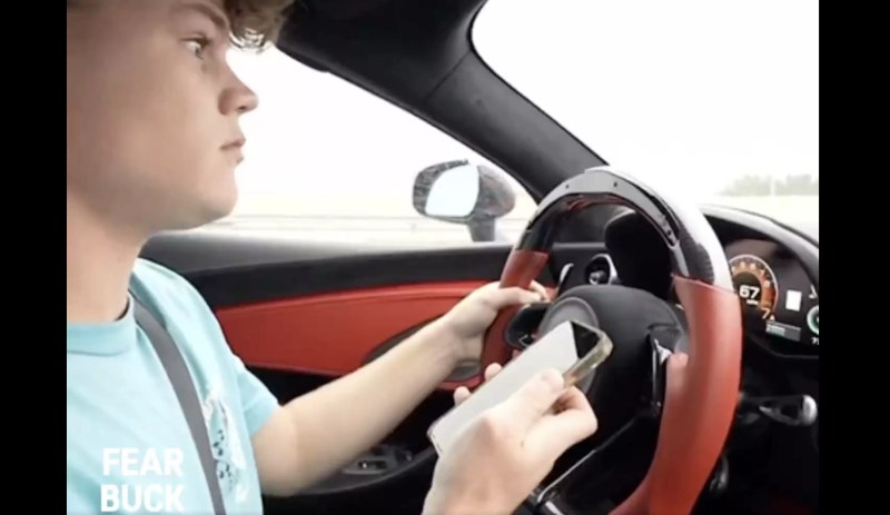 Jack Doherty sitting behind the wheel of his McLaren and holding his cellphone in his right hand