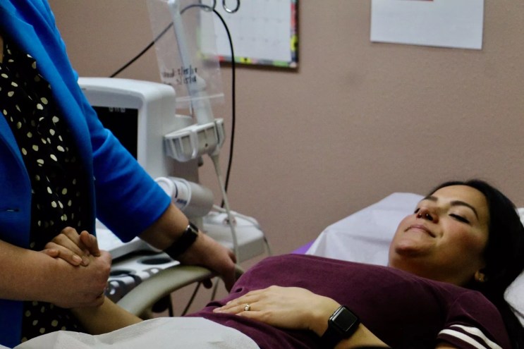 A woman holds a doctor's hand as she lies on an examining room table.