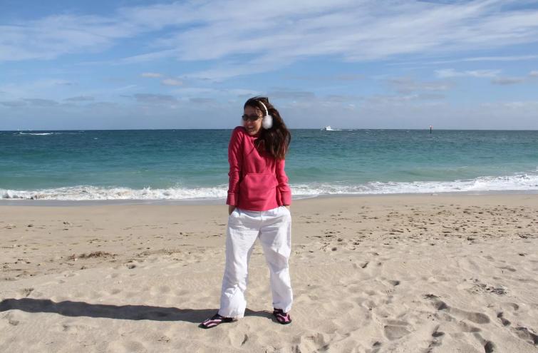 stock photo of woman smiling while wearing winter earmuffs with ocean background