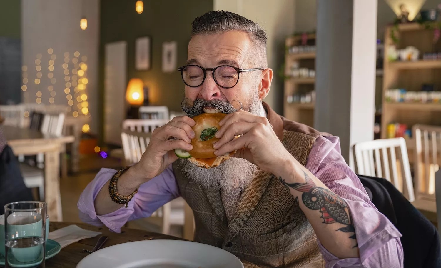 Mature man sitting at a table in a cafe in Newcastle-upon-Tyne, eating a vegan bagel.