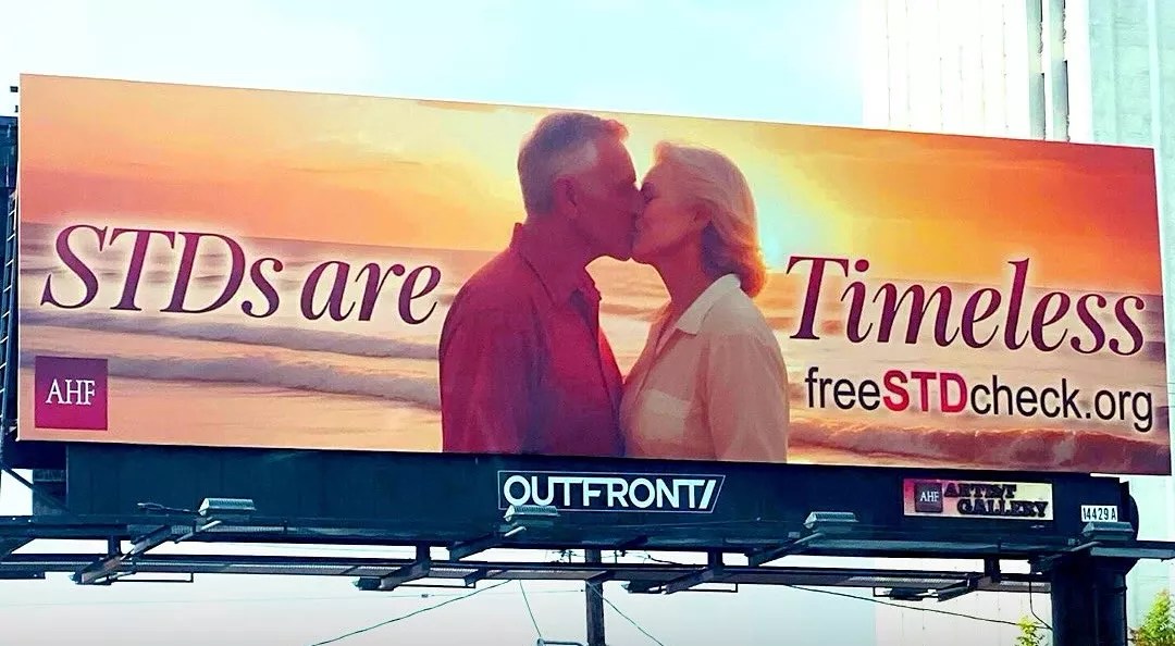 A billboard shows two seniors, a man and a woman, kissing and text that reads "STDs are Timeless"