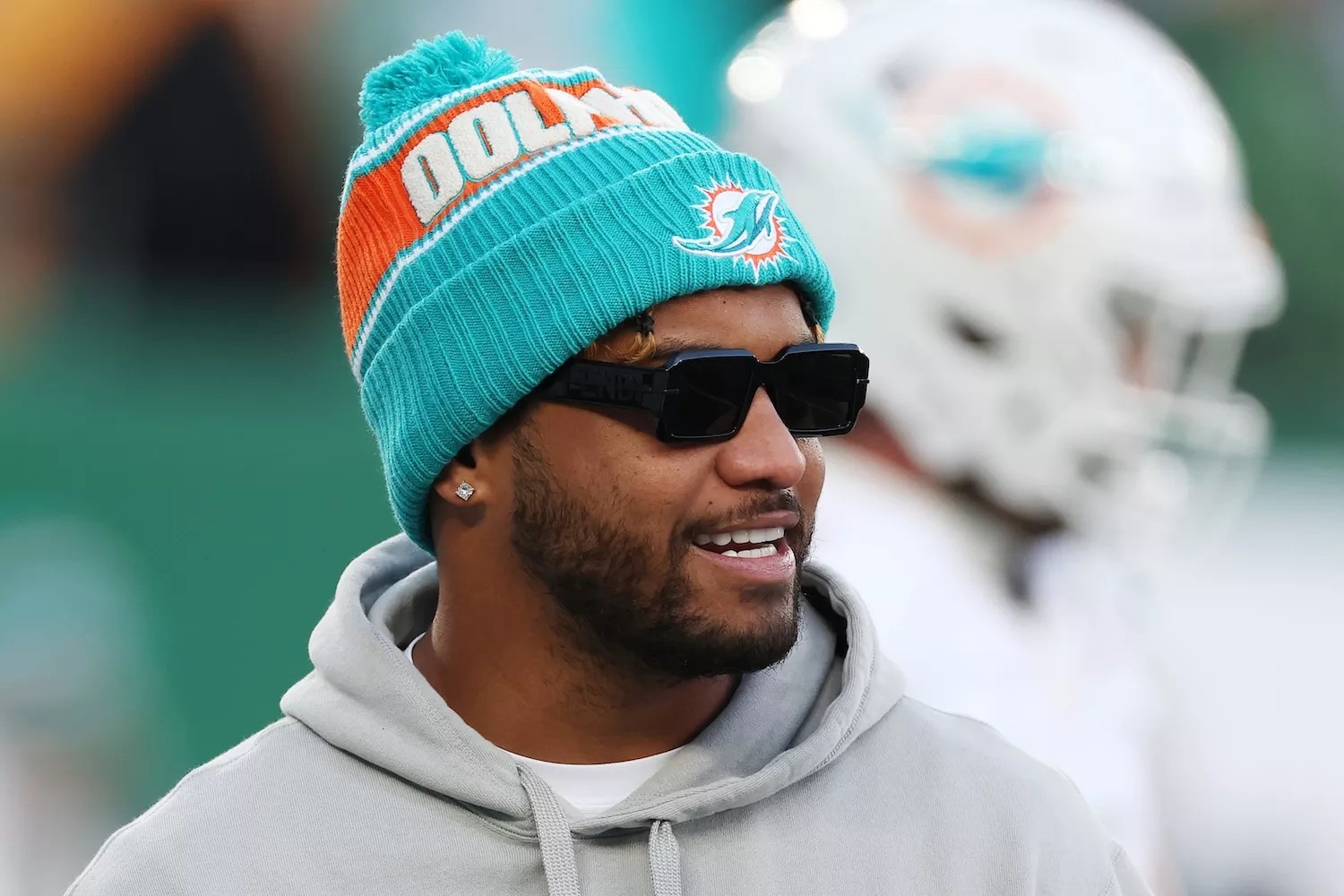 Sporting sunglasses and a pom-pom-topped team-issue knit hat, Tua Tagovailoa #1 of the Miami Dolphins looks on before the game against the New York Jets at MetLife Stadium on January 05, 2025, in East Rutherford, New Jersey