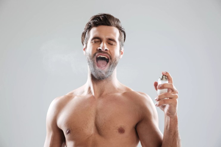 A shirtless man enthusiastically spraying himself with cologne, mouth open wide, highlighting excessive fragrance habits discussed in Miami