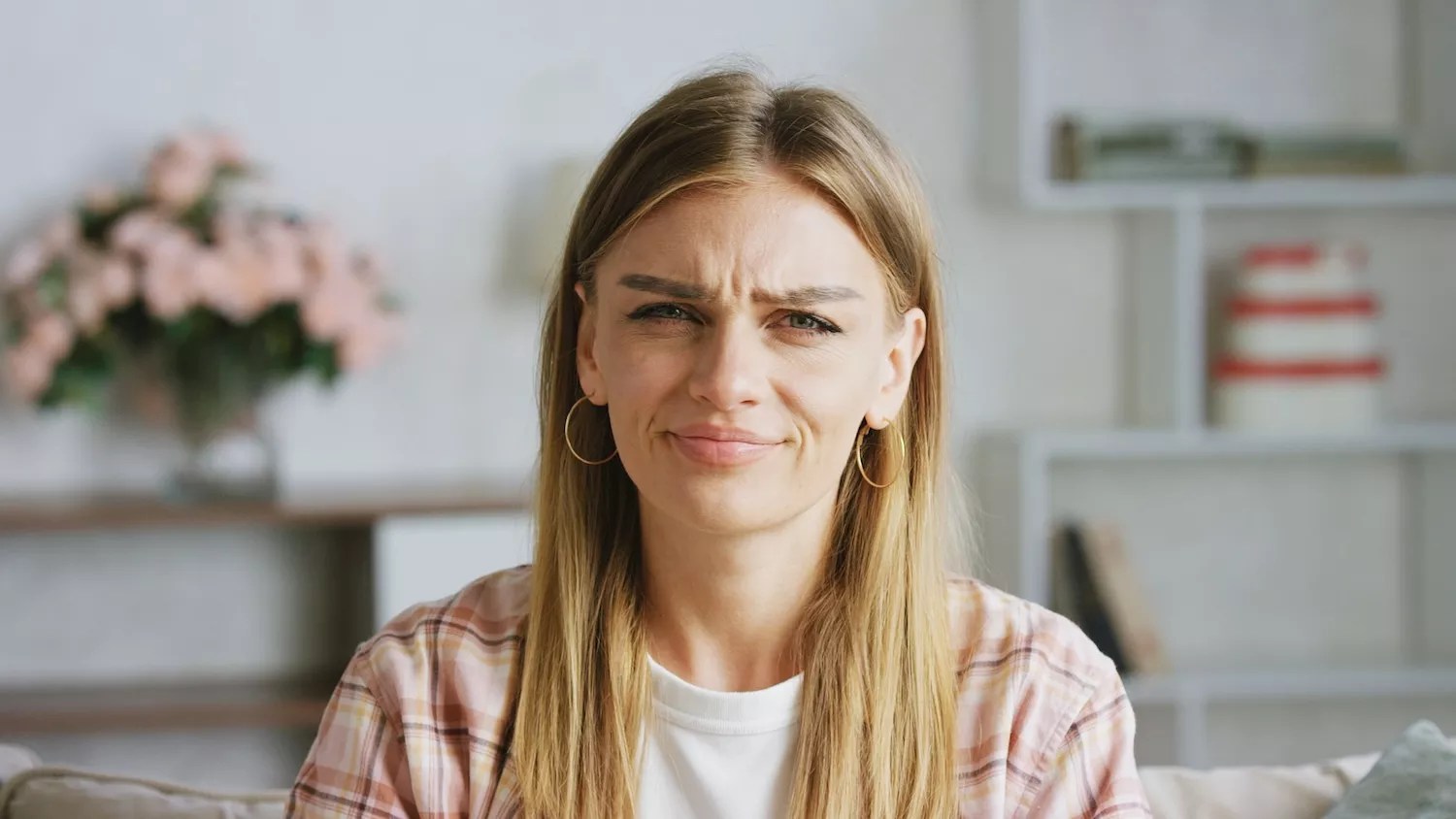 Young woman wearing casual clothes frowning on a sofa in her living room, expressing clear disgust and disapproval, reflecting negative emotions and frustration