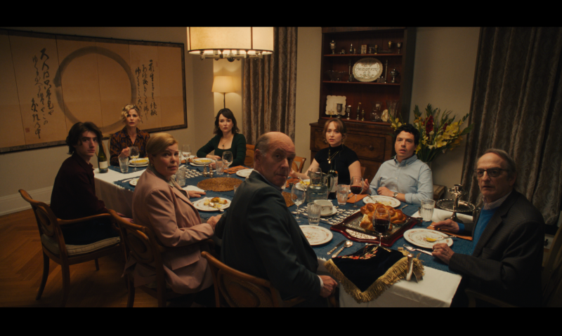 a film still of eight family members gathered around the dinner table glaring at the camera in unison