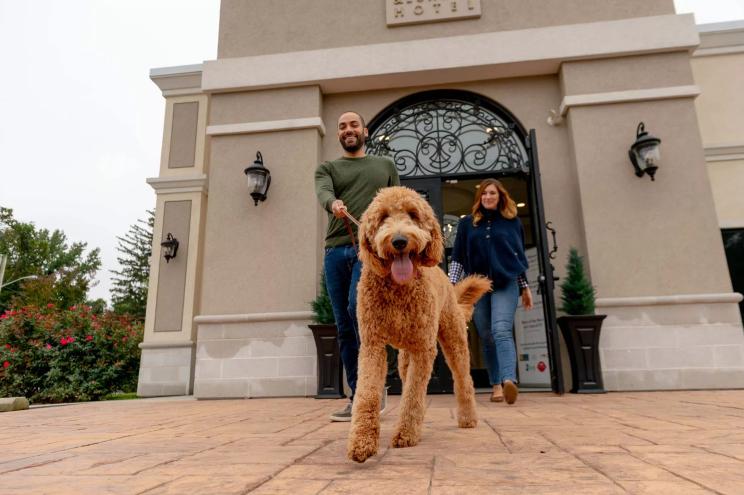 two people walk a dog outside a hotel