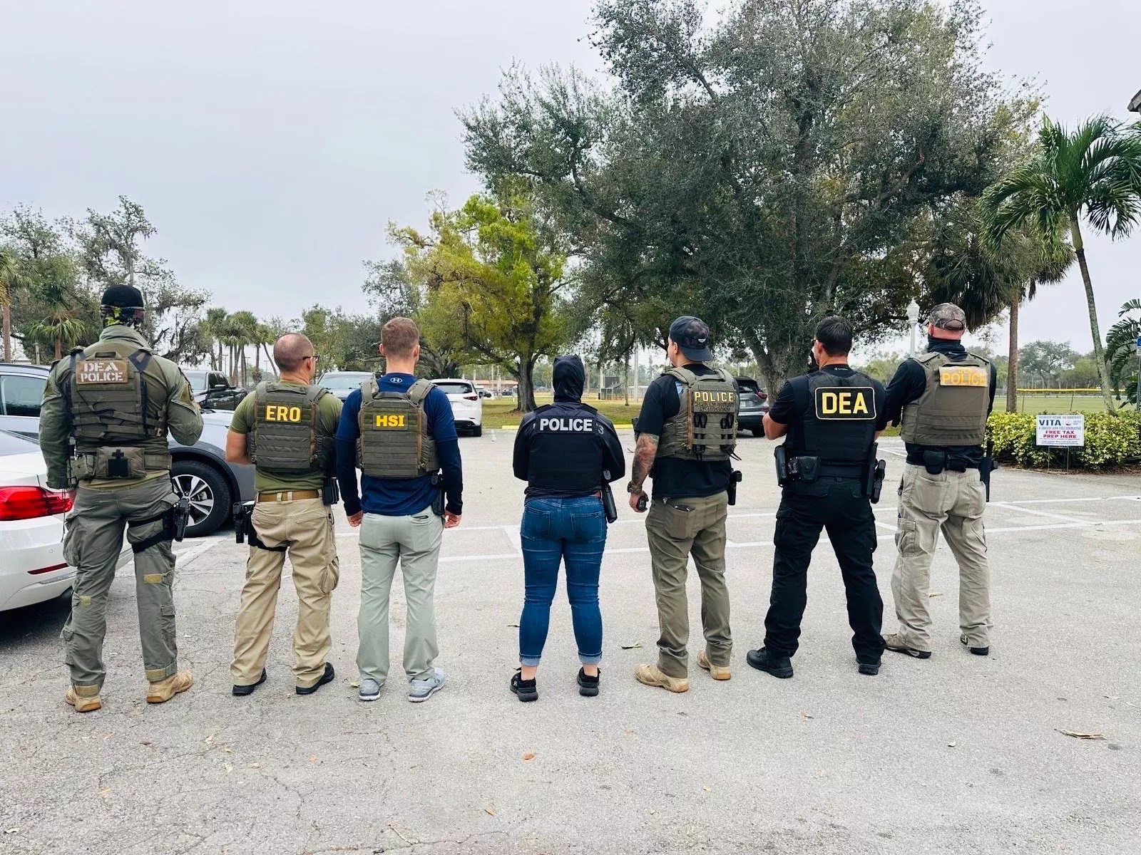 HSI, ICE, and DEA agents stand in a line with their backs to the camera.