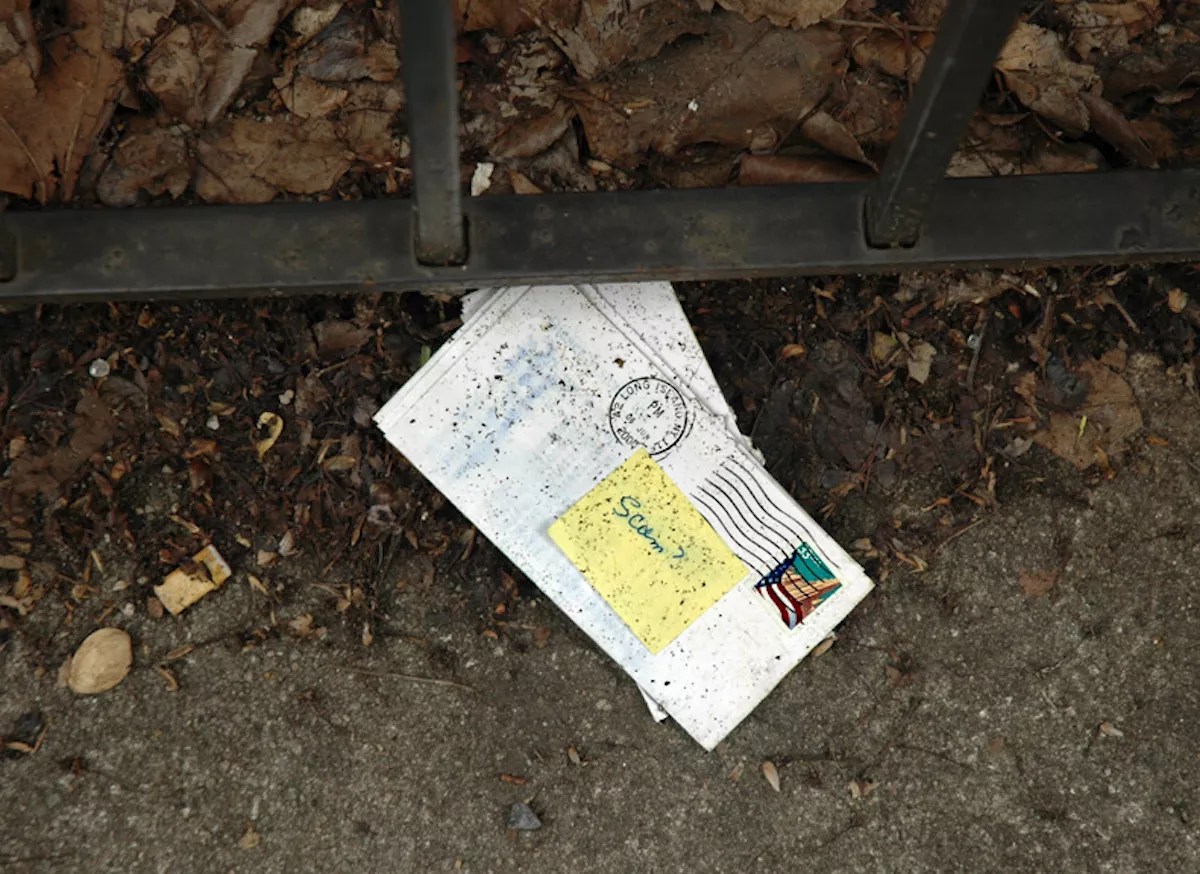 An envelope on the floor with a sticky note on top that reads "Scam?"