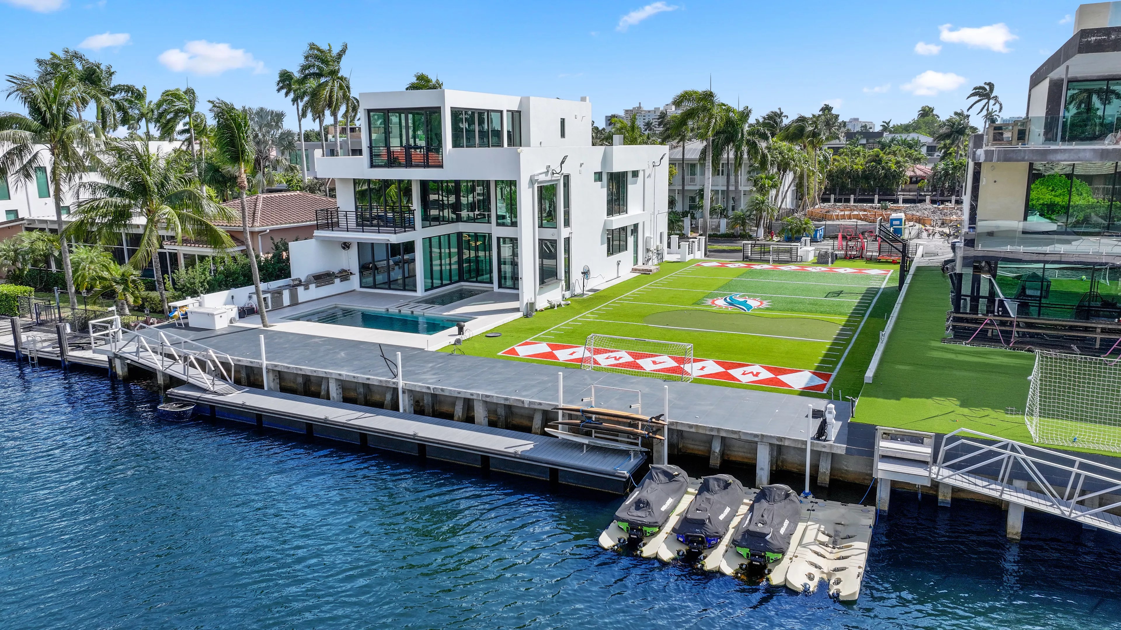 Waterfront white mansion with Miami Dolphins football field next to it