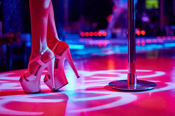 A woman's feet in high heels near a stripper pole with garish lighting