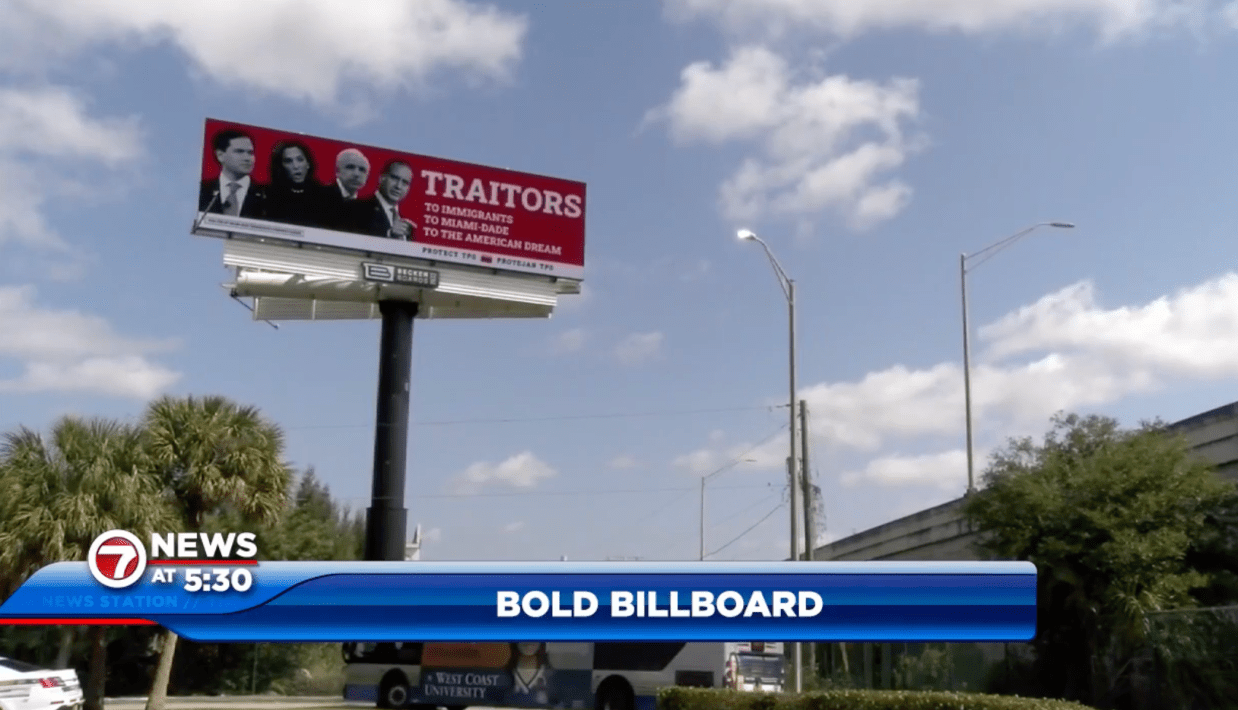 A photo of a red billboard with four politicians on it and the words: “TRAITORS: To Immigrants, To Miami-Dade, To The American Dream” above a blue sky