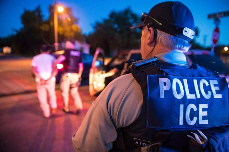 An ICE Enforcement and Removal Operations (ERO) officer arrests someone as another officer looks on