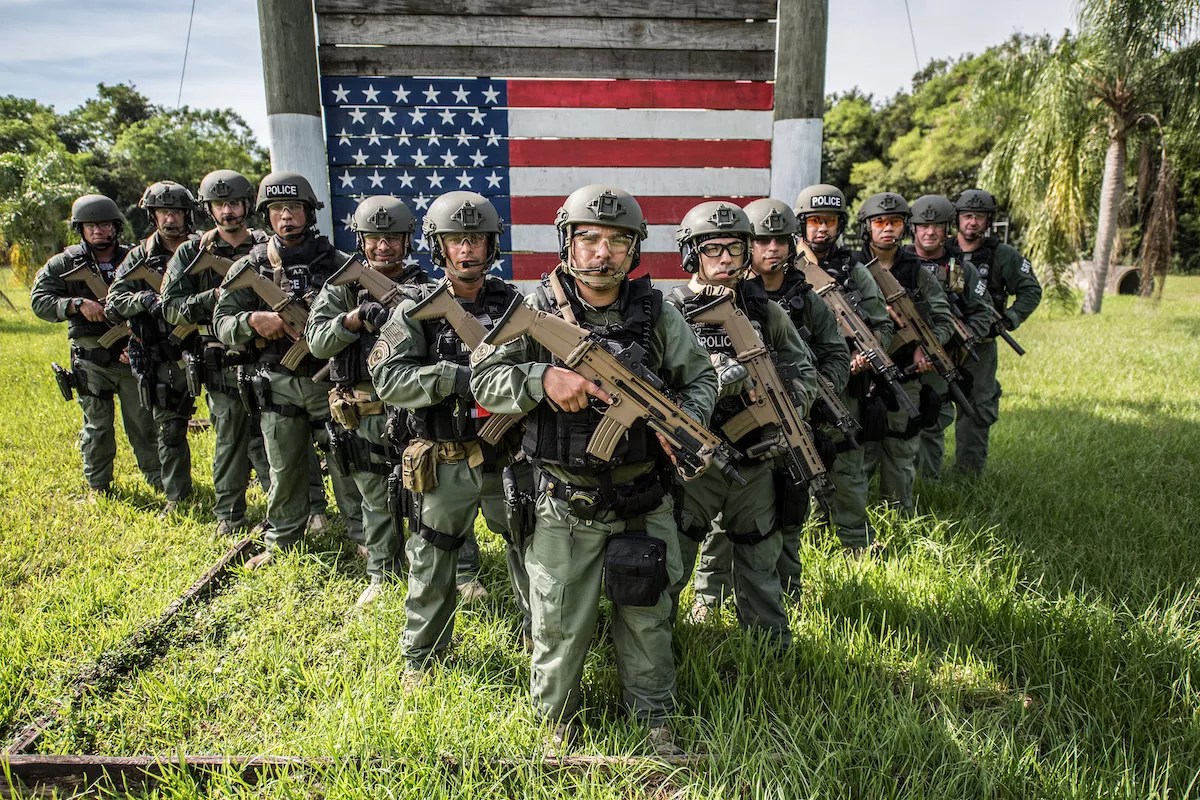 Armed and uniformed U.S. Immigration and Customs Enforcement (ICE) officers standing in the grass in Miami.