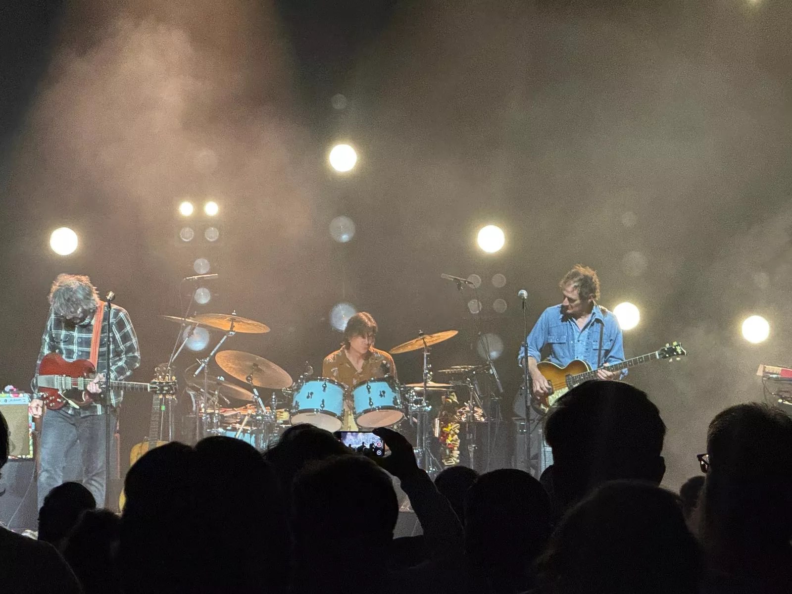 A rock band on stage, rocking, with the silhouettes of audience members in the foreground