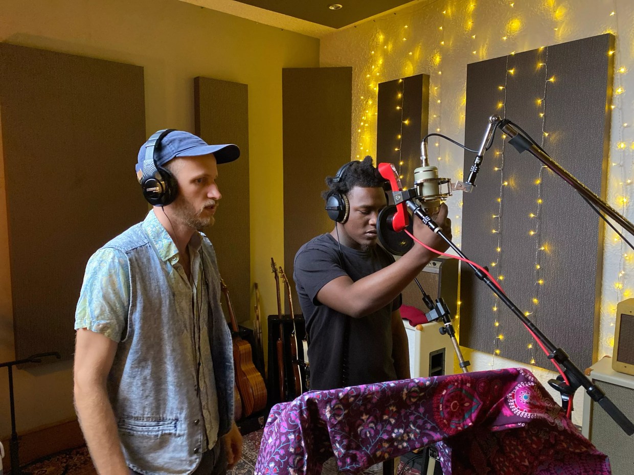 two men, one white, the other Black, wearing headphones in a modest recording studio