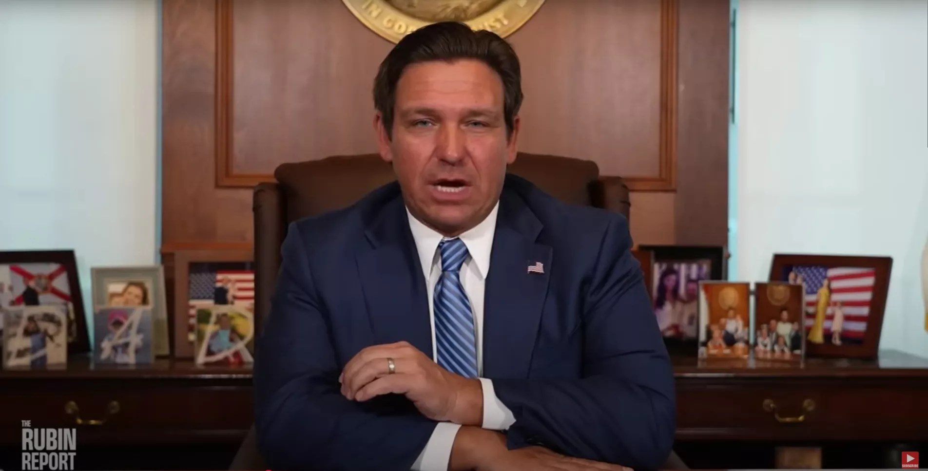 Ron DeSantis wearing a blue tie sitting at his desk