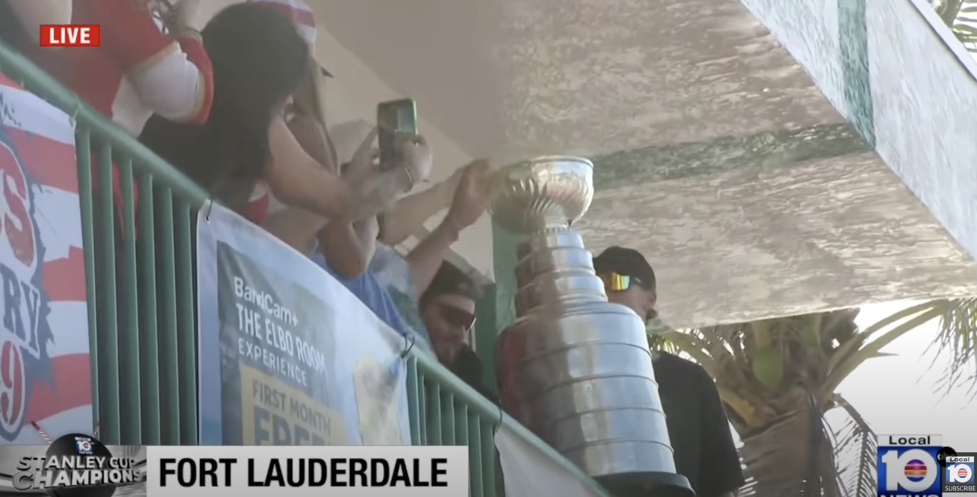 Florida Panthers players hold the Stanley Cup on a balcony, surrounded by fans