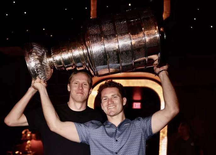 two members of the NHL's Florida Panthers hoisting the 2025 Stanley Cup trophy inside a restaurant
