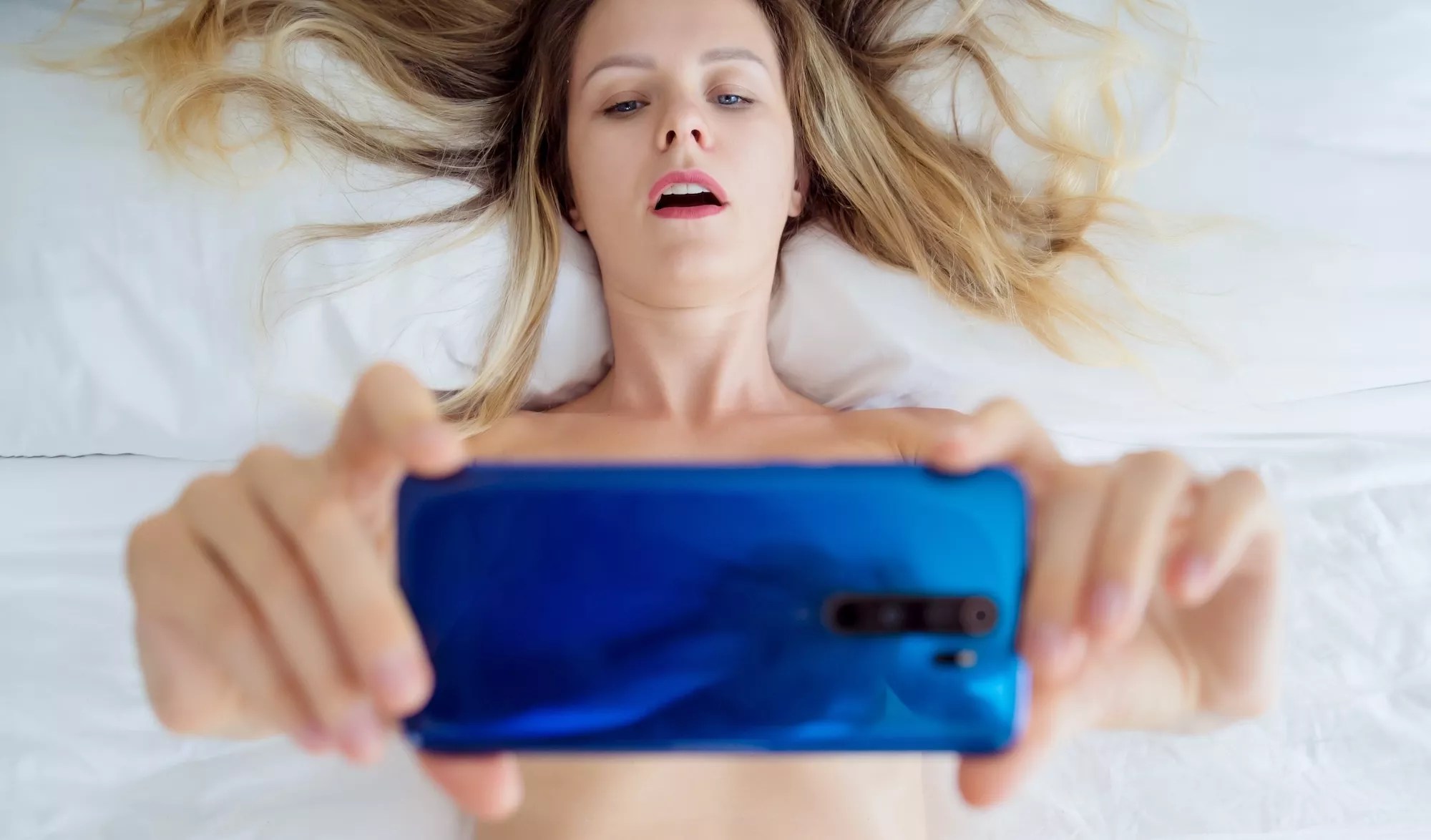 Young sexy woman posing in front of smartphone in his hand and working as webcam model