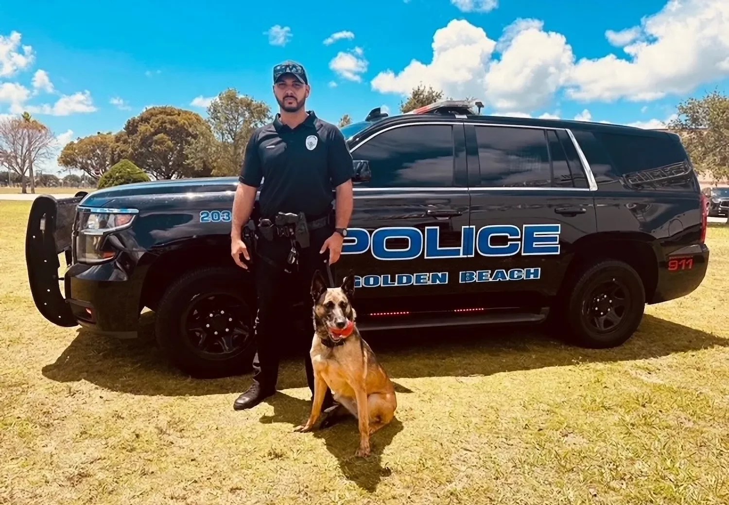 uniformed police officer standing with his K-9 in front of a black police cruiser