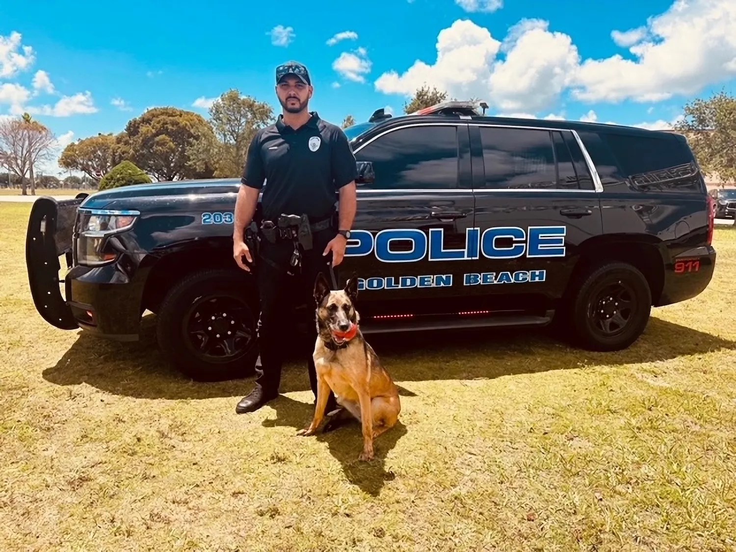 uniformed police officer standing with his K-9 in front of a black police cruiser