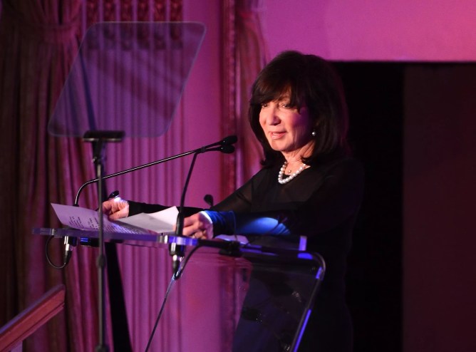 photo of a woman standing at a podium and speaking into a microphone