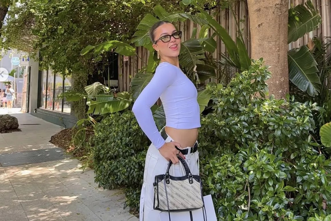 a young girl poses with a purse in front of greenery