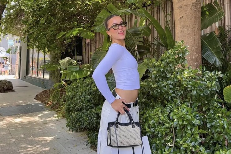 a young girl poses with a purse in front of greenery