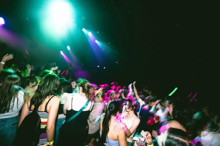A group of young people dancing in a club. under green and fuchsia lights.