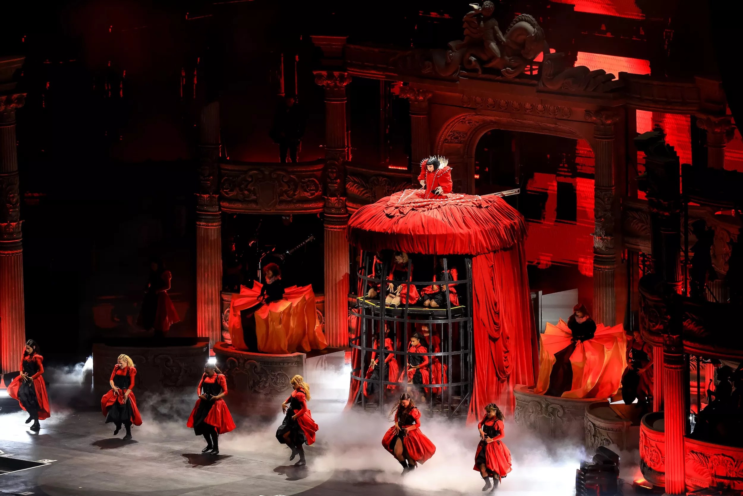 Image of Lady Gaga on stage wearing a red dress that also serves as a cage.
