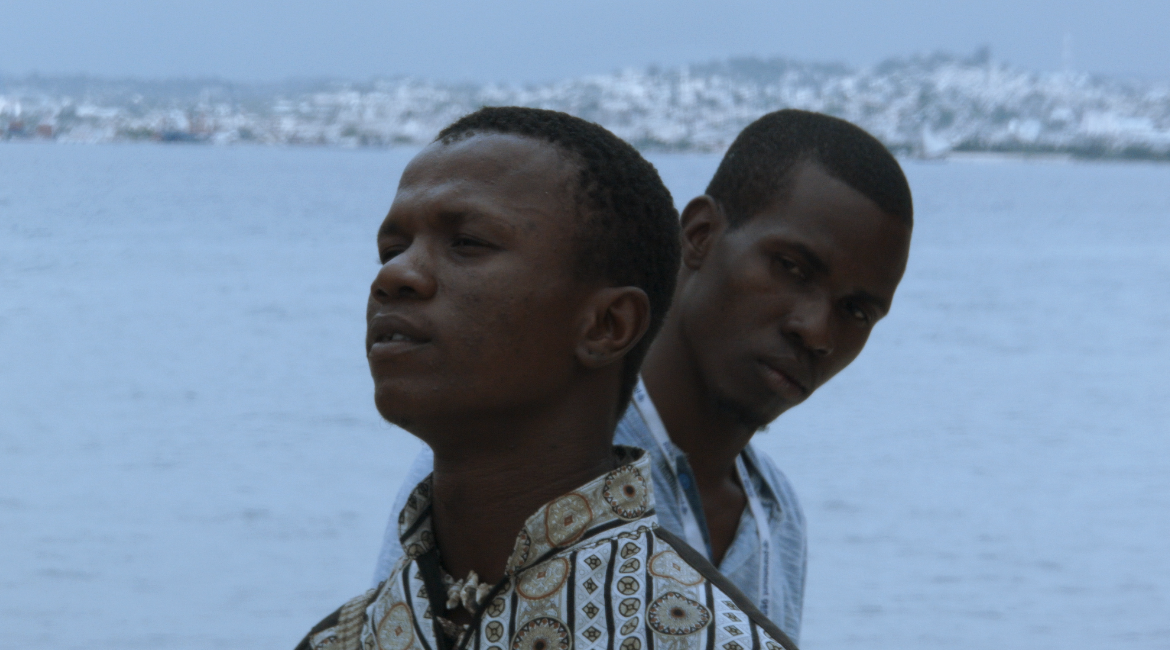 a still from a film showing a close-up of a Black man standing behind another