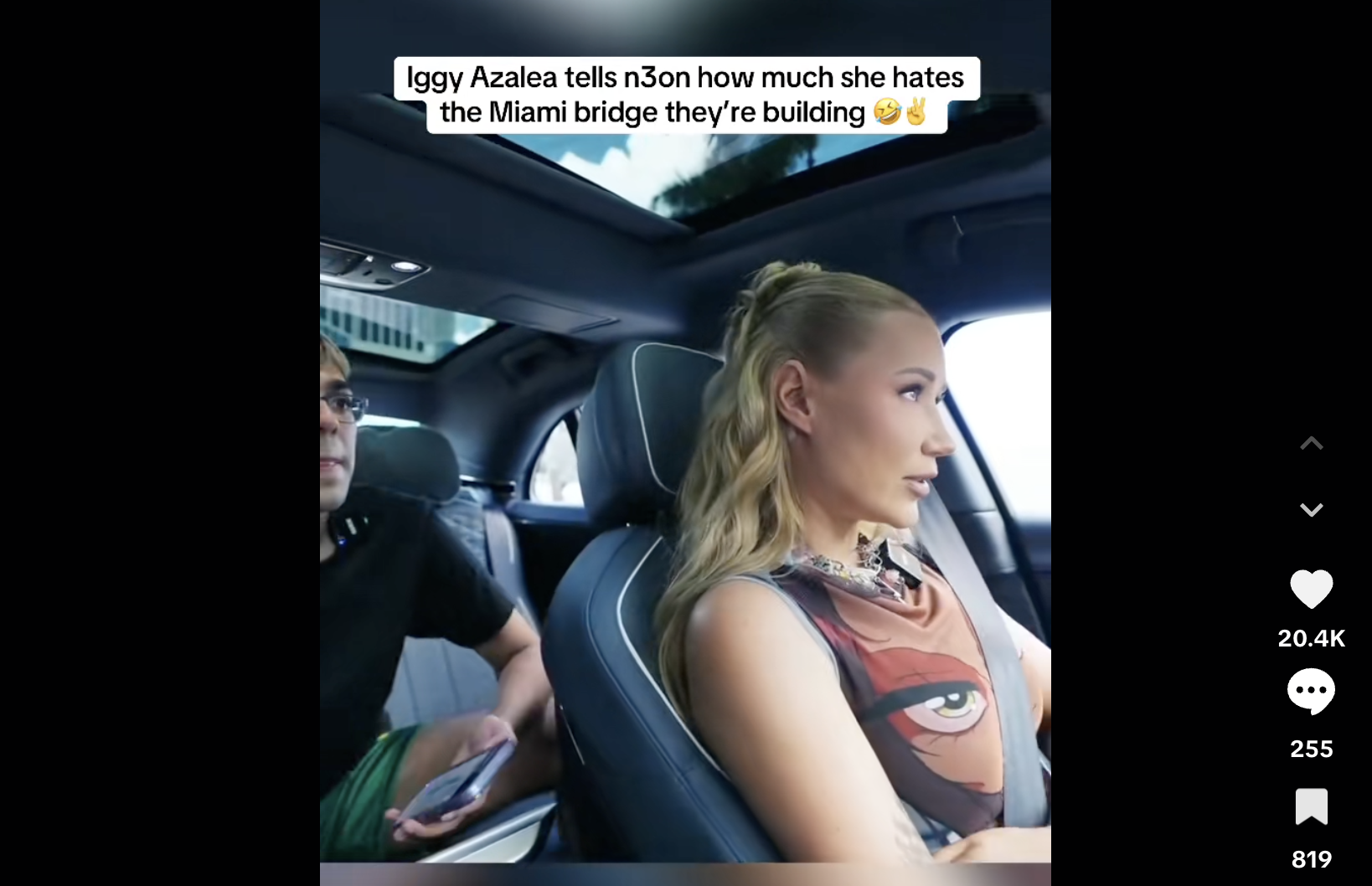 Screenshot of a TikTok video showing livestreamer N3on in the back of a car being driven by rapper Iggy Azalea. Text overlayed over the image reads, "Iggy Azalea tells N3on how much she hates the Miami bridge they're building 🤣✌️"
