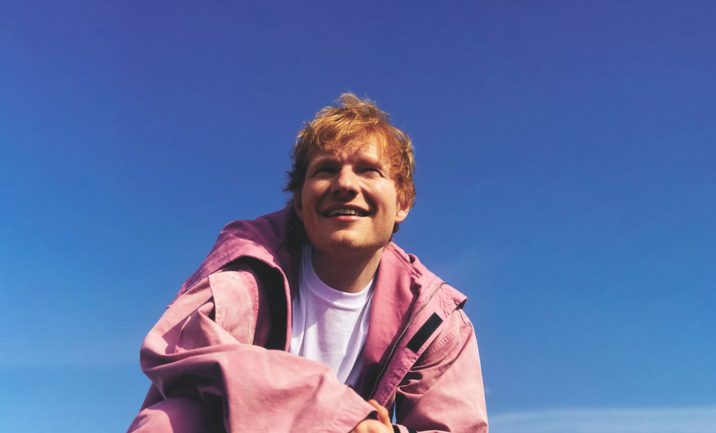Picture or a man with the sky as background and wearing a pink hoodie.